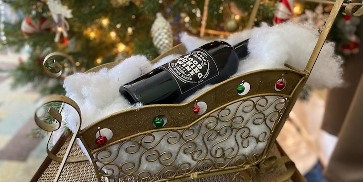 A bottle of red wine inside a decorative sled in front of a Christmas tree